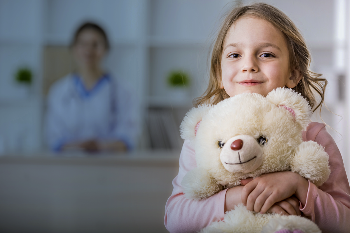 stock-photo-little-girl-with-teddy-bear-is-looking-at-the-camera-female-doctor-on-background-1200x800.png